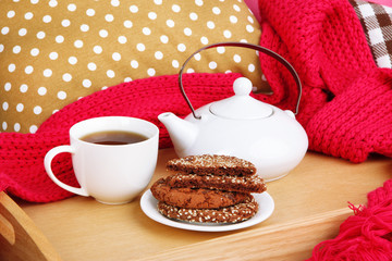 Cup and teapot with cookies on tray and scarf on bed close up