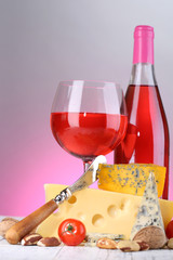 Pink wine and different kinds of cheese on colorful background