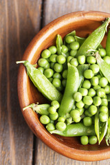 Green peas in wooden bowl on wooden background