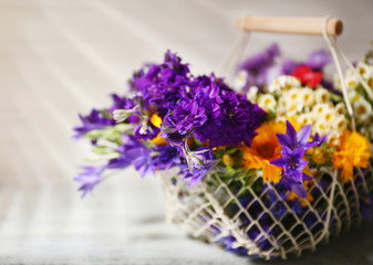 Beautiful wild flowers in basket on wooden background