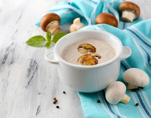 Mushroom soup in white pot, on napkin,  on wooden background
