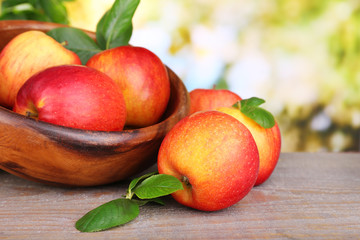 Ripe sweet apples with leaves in wooden bowl,