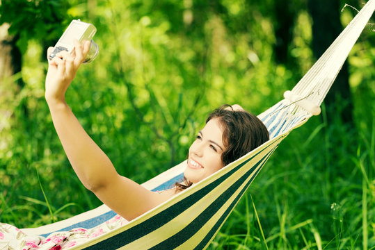 Young woman in a hammock in garden doing snapshot.