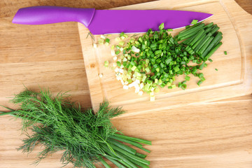 Chopped green onion with knife on cutting board on wooden table