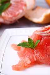 Ripe peeled grapefruits on plate, on color wooden background