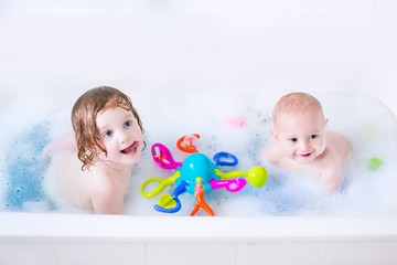 Two little kids playing in a bath tub with toys