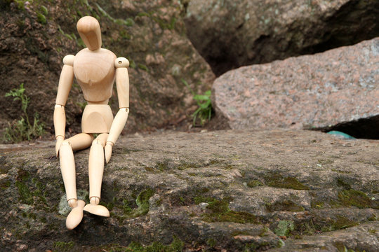 Wooden pose puppet sitting on stone, outdoors