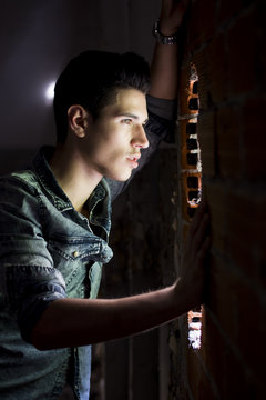 Young Man Looking Through Hole In Brick Wall