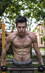 Handsome shirtless young man exercising in outdoor gym in park