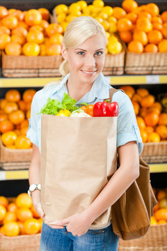 Girl hands bag with fresh vegetables in supermarket