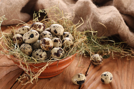 quail eggs in a clay bowl with hay on the background of wooden p