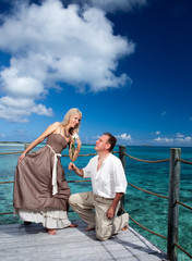 Loving couple on a wooden platform over sea on tropical island..