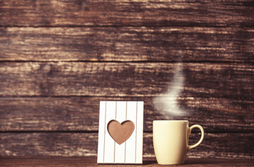 Frame with heart shape and cup of coffee on wooden background.