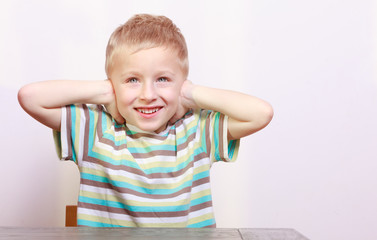 Portrait of blond boy child kid covering ears at the table