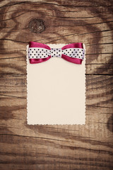 blank paper sheet with pink and white polka dot bow on wooden ba