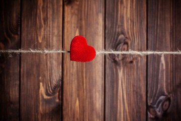 red fabric heart hanging on clothesline against wooden backgroun