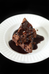 Slices of brownie on white plate covered with chocolate