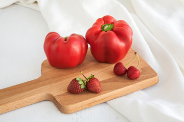 Red peppers ,strawberries and cherries on wood and white fabric