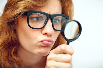 Young geek looking through magnifying glass.