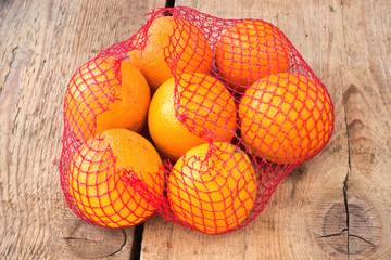 Fresh oranges in plastic net on wooden background © gavran333