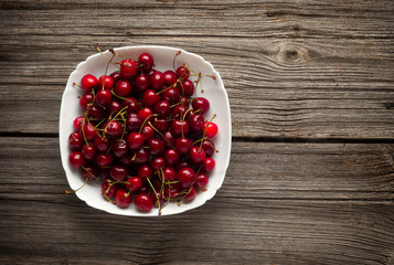 Bowl of ripe cherries on a wooden background