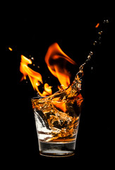 Glass with whiskey splash and fire on black background