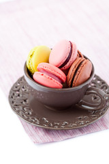 Colorful macaroons in brown cup on white background