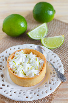 Lemon tart pie on white plate spoone on sackcloth with fresh lim