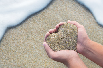 Hands holding a sand in form of the heart with text 