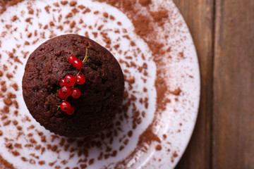 Chocolate muffin with red currant on plate on wooden background