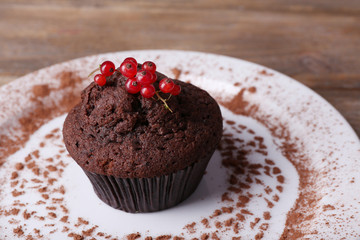Chocolate muffin with red currant on plate on wooden background