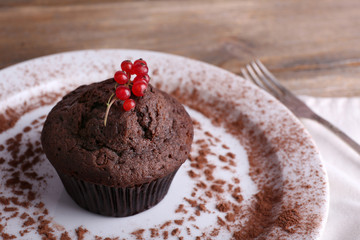Chocolate muffin with red currant on plate on wooden background