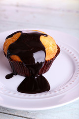 Tasty muffin with chocolate sauce on plate, on bright