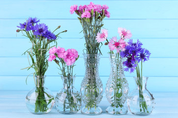 Beautiful summer flowers in vases on blue wooden background