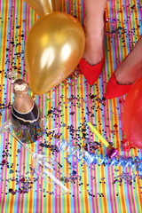 Legs with confetti, champagne and balloons on the floor