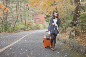 秋の紅葉した公園でトランクを引いている女性