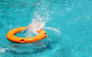 Orange life buoy is splashing with clear blue water in swimming