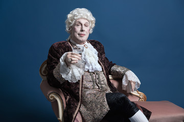 Retro baroque man with white wig holding a wine glass sitting on