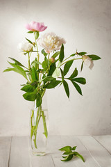 A  bouquet of  pale peonies in a glass vase on wooden table.