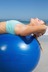 Fit woman lying on exercise ball at the beach stretching