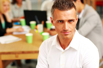 Portrait of happy businessman sitting in front of colleagues