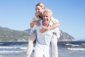 Man giving his laughing wife a piggy back at the beach
