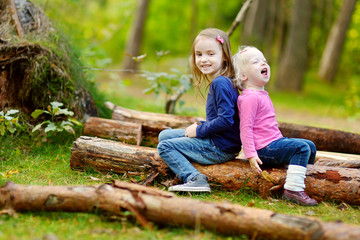 Naklejka na ściany i meble Two little sisters sitting on a log in a forest