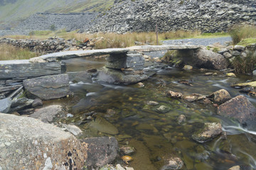 Old stone clapper bridge over mountain stream.