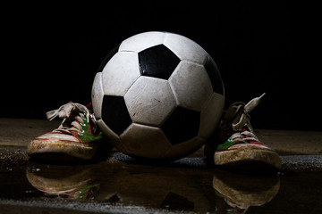 Dirty sneakers with soccer ball on black background
