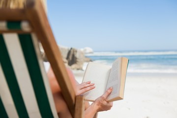 Woman sitting in deck chair at the beach reading