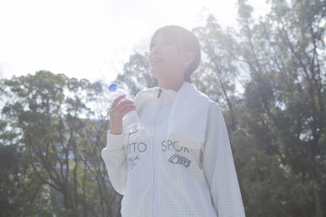 公園で首からタオルをかけてペットボトルを持つ女性