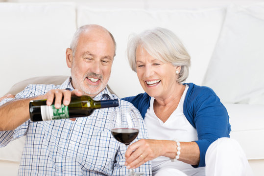 glückliches seniorenpaar schenkt sich wein ein