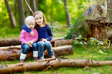 Two little sisters sitting on a log in a forest