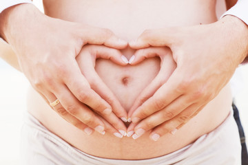 A couple making a heart shape on the pregnant belly with hands - obrazy, fototapety, plakaty